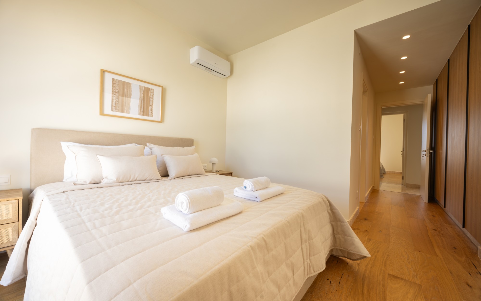 A made-up bedroom with fresh towels folded on the bed and warm oak flooring.